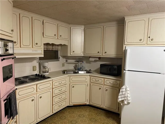 Kitchen with tasteful backsplash, white fridge, dark tile flooring, sink, and electric cooktop