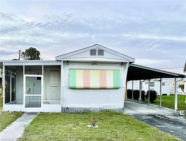 Manufactured / mobile home featuring a sunroom, a front yard, and a carport