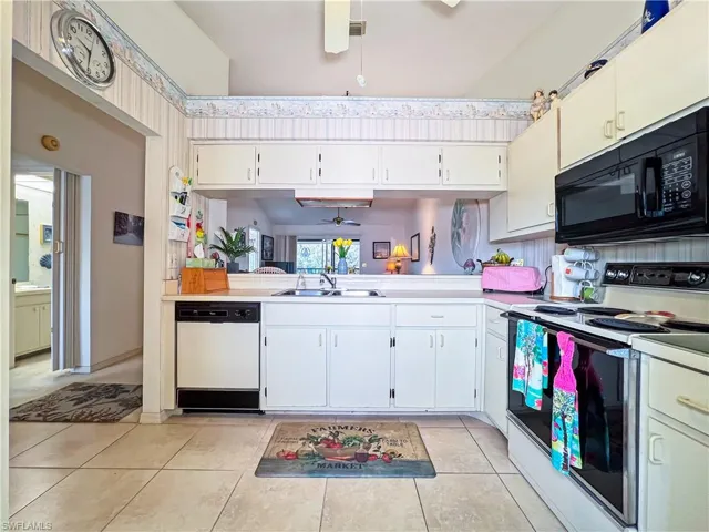 Kitchen featuring sink, white appliances, ceiling fan, light tile patterned floors, and white cabinets