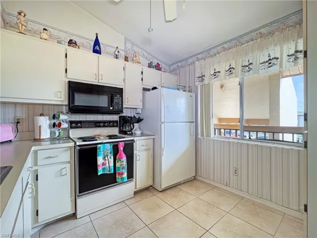 Kitchen featuring light tile patterned floors, white appliances, vaulted ceiling, and white cabinets