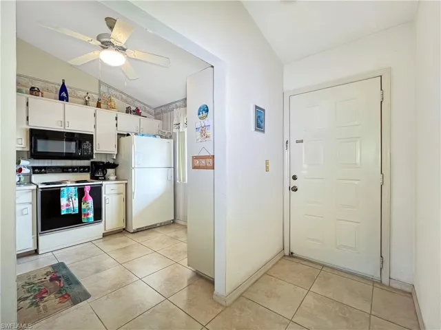 Kitchen featuring white appliances, light tile patterned floors, vaulted ceiling, ceiling fan, and white cabinets