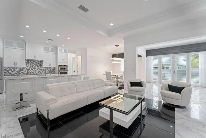Open-concept living space featuring a modern kitchen with white cabinetry, a mosaic tile backsplash, and stainless steel appliances