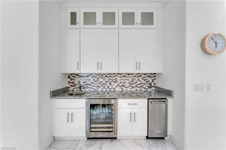 Wet bar featuring white shaker cabinetry, glass-front upper cabinets, a honeycomb tile backsplash, and a granite countertop