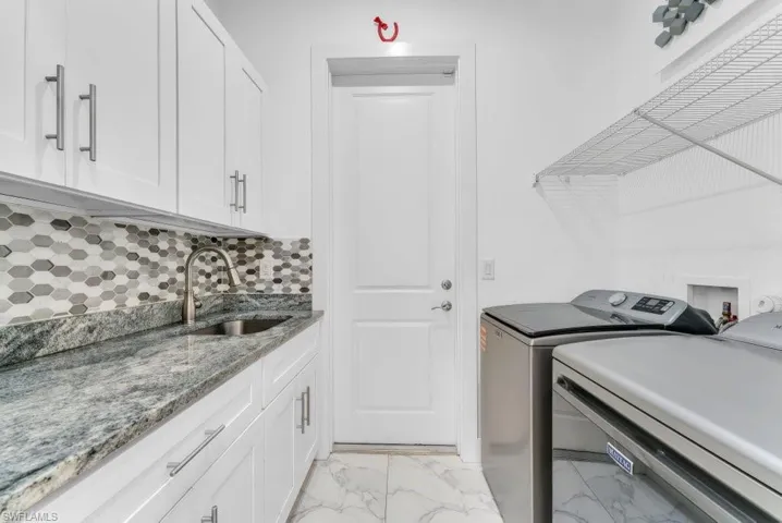 Laundry room featuring white cabinetry, a large sink, stone countertop, hexagon tile backsplash, and tile flooring