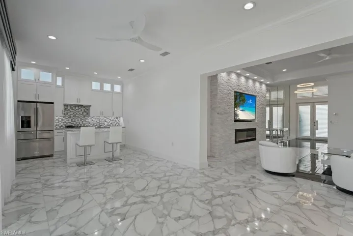 Open concept living space featuring large format porcelain tile flooring, a contemporary kitchen with white cabinetry and stainless steel appliances, a stone accent wall with an integrated fireplace and television mount, and recessed lighting throughout