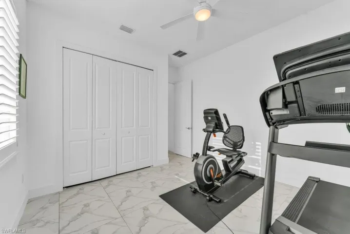 Room featuring large format marble-look floor tiles, a window with white louvered shutters, bi-fold closet doors, and an overhead ceiling fan with integrated lighting