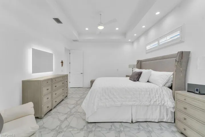 Spacious bedroom featuring contemporary marble-look tile flooring, a tray ceiling with recessed lighting, and a modern ceiling fan