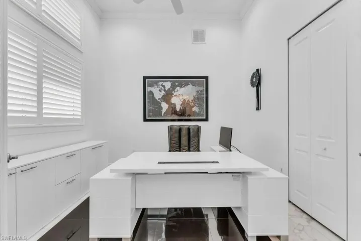 Dedicated office space featuring built-in cabinetry with modern pulls, plantation shutters, and a ceiling fan