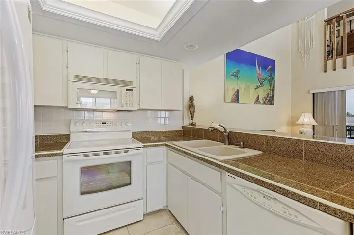 Kitchen featuring white cabinets, tile counters, a sink, white appliances, and tasteful backsplash