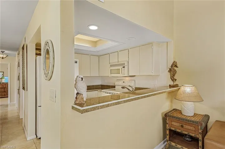 Kitchen featuring a peninsula, a tray ceiling, white appliances, and light tile patterned floors
