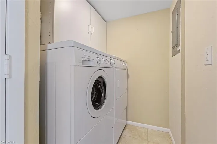 Laundry area featuring cabinet space, washing machine and clothes dryer, baseboards, and light tile patterned floors