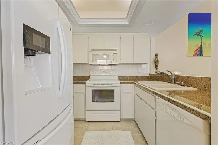 Kitchen featuring a sink, tile countertops, white appliances, a tray ceiling, and backsplash