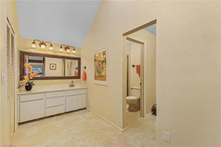Bathroom with toilet, vanity, baseboards, lofted ceiling, and tile patterned flooring