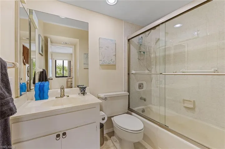 Full bathroom with enclosed tub / shower combo, toilet, vanity, and visible vents