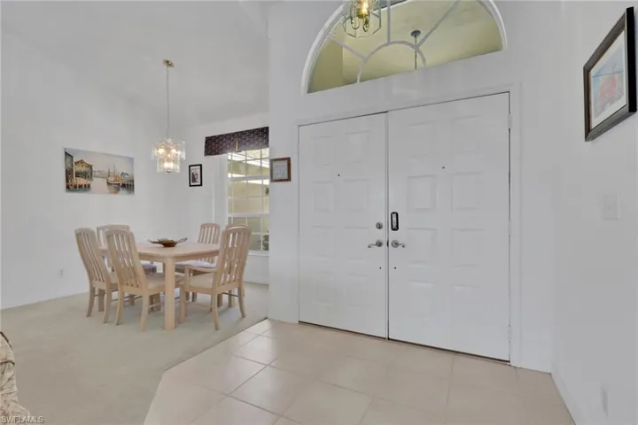 Foyer featuring a chandelier, light colored carpet, light tile patterned floors, and high vaulted ceiling