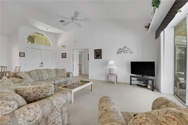 Carpeted living area with high vaulted ceiling and a ceiling fan