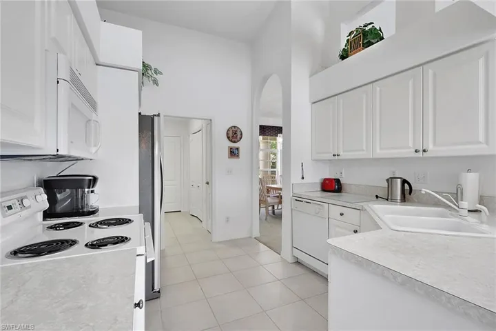 Kitchen featuring a towering ceiling, white cabinetry, white appliances, light countertops, and arched walkways