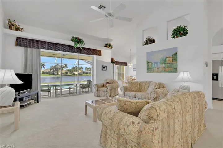 Living area with a ceiling fan, light colored carpet, high vaulted ceiling, and a sunroom