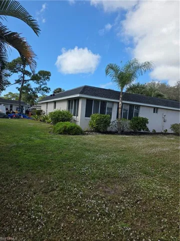 View of side of home with stucco siding, a yard, a sunroom, and a shingled roof