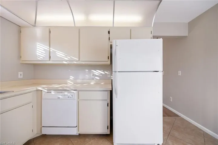 Kitchen with white appliances, light countertops, light tile patterned floors, and white cabinets