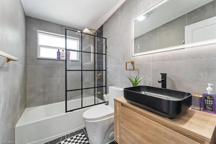 Full bathroom featuring tile patterned flooring, toilet, shower / bath combination with glass door, vanity, and tile walls