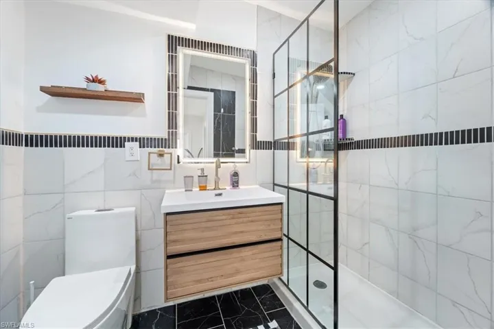 Bathroom with toilet, a tile shower, tile walls, and vanity