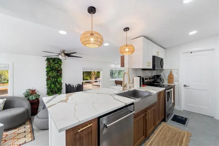 Kitchen featuring decorative backsplash, appliances with stainless steel finishes, sink, white cabinets, and hanging light fixtures