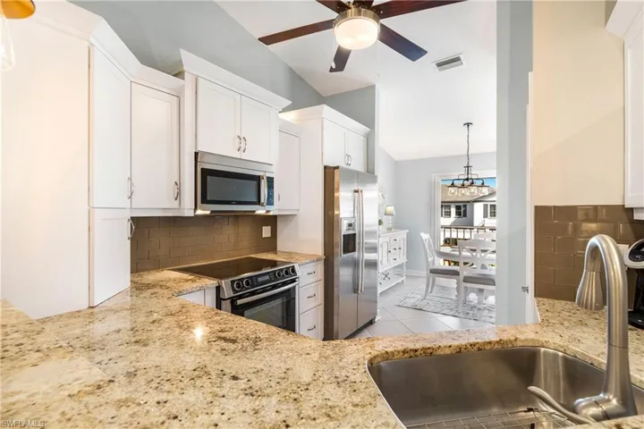 Kitchen featuring decorative light fixtures, backsplash, stainless steel appliances, light stone counters, and vaulted ceiling