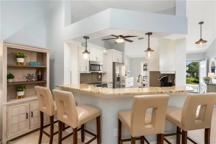 Kitchen featuring hanging light fixtures, a kitchen breakfast bar, appliances with stainless steel finishes, light stone countertops, and tasteful backsplash