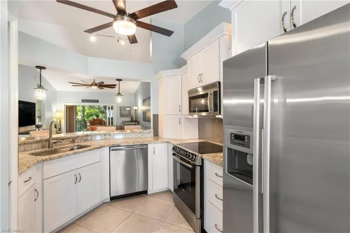 Kitchen with stainless steel appliances, white cabinetry, light stone countertops, open floor plan, and vaulted ceiling