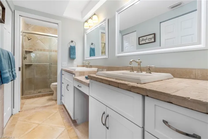Bathroom with double vanity, a shower stall, and light tile patterned floors