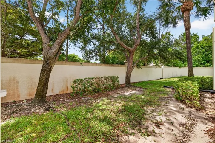 Landscaped outdoor area featuring a stucco privacy wall, mature trees, manicured shrubs, and a grassy lawn