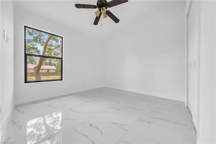 Empty room featuring light marble finish floors, a ceiling fan, and vaulted ceiling