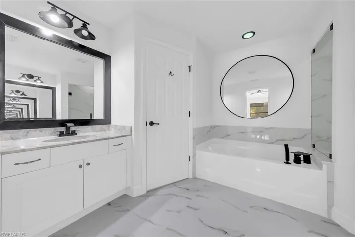 Full bath featuring a bath, vanity, light marble finish floors, and recessed lighting