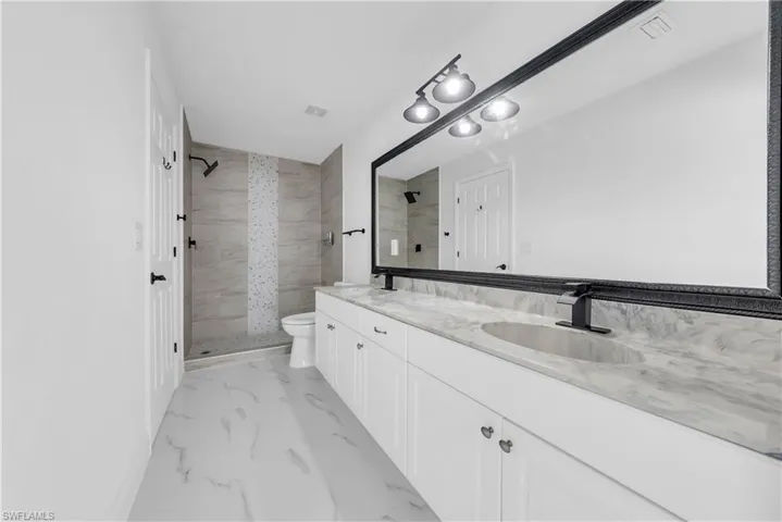 Bathroom featuring tiled shower, double vanity, and light marble finish floors
