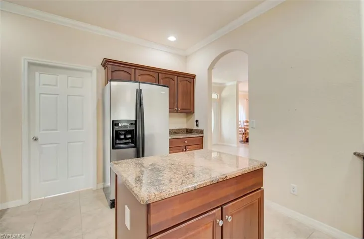 Kitchen featuring light stone counters, ornamental molding, stainless steel fridge, and light tile flooring