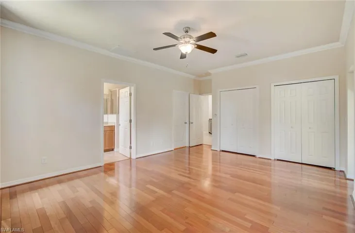 Unfurnished bedroom featuring ceiling fan, light wood-type flooring, ensuite bathroom, and ornamental molding