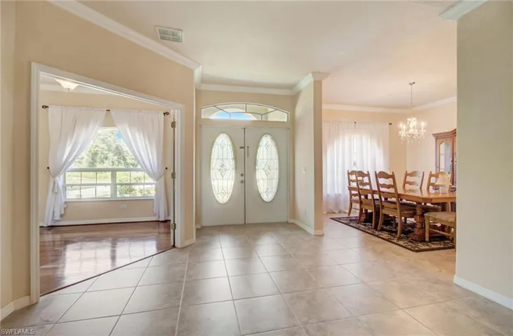 Tiled foyer with crown molding, french doors, and an inviting chandelier