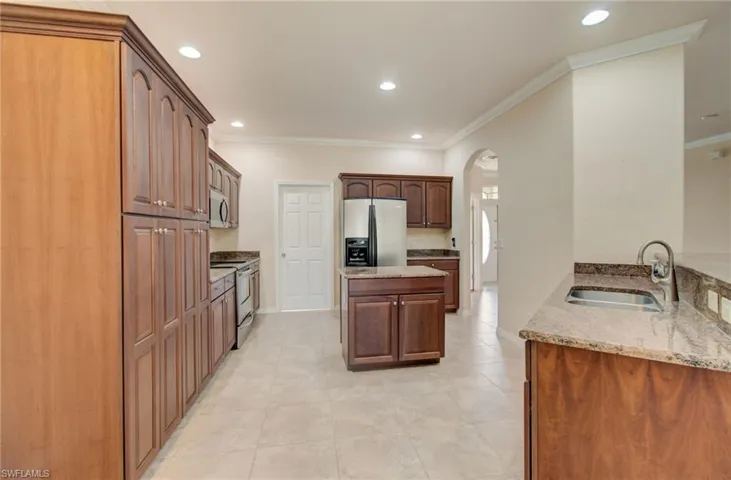 Kitchen with stainless steel appliances, light stone counters, sink, and light tile floors