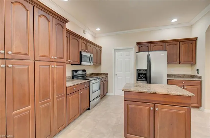 Kitchen featuring stainless steel appliances, crown molding, a center island, light stone countertops, and light tile floors