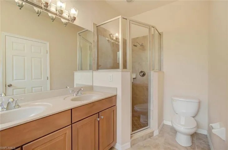 Bathroom featuring dual vanity, toilet, tile floors, and a shower with door