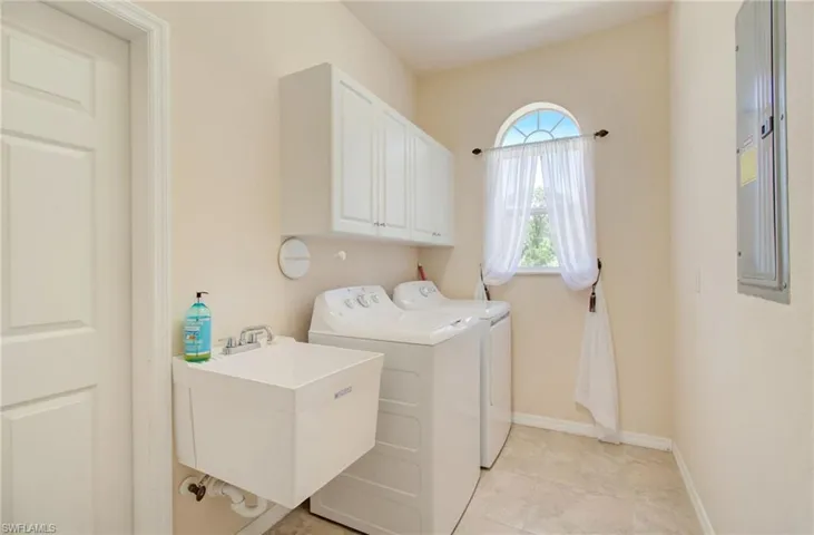 Clothes washing area featuring sink, washer and dryer, cabinets, and light tile floors