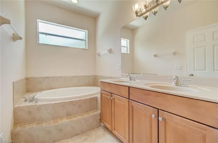 Bathroom featuring a relaxing tiled bath, dual bowl vanity, tile flooring, and plenty of natural light