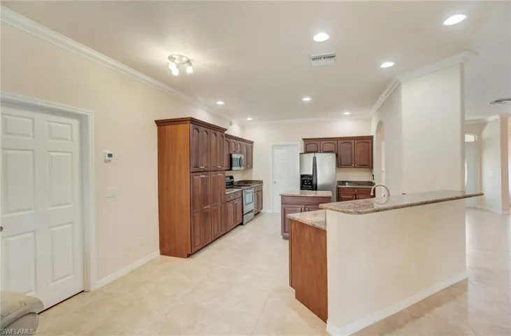 Kitchen featuring an island with sink, light stone counters, light tile floors, ornamental molding, and appliances with stainless steel finishes