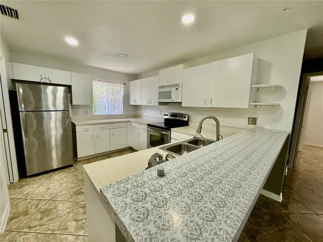 Kitchen featuring stainless steel appliances, light countertops, white cabinets, a peninsula, and recessed lighting