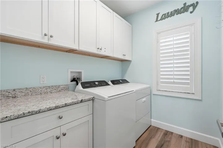 Laundry room with wood-finish flooring, white cabinetry, and a light-toned countertop - Virtually Edited Image
