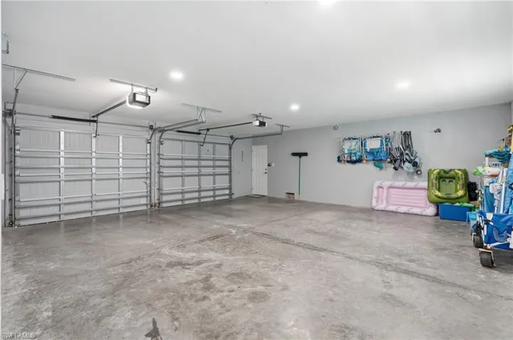 Two-car garage featuring a concrete floor, two automatic garage door openers, and recessed lighting - Virtually Edited Image