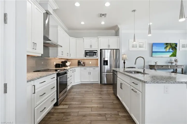 Kitchen featuring white cabinetry, stainless steel appliances, granite countertops, tile backsplash, and wood-finish flooring - Virtually Edited Image