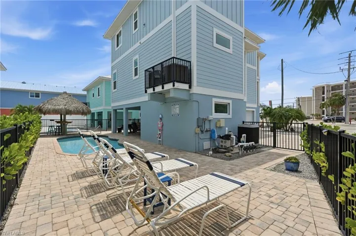 Paver patio with a built-in swimming pool, surrounded by a black metal fence and mature landscaping - Virtually Edited Image