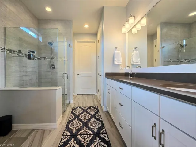 Bathroom featuring double vanity, a stall shower, wood finish floors, and recessed lighting